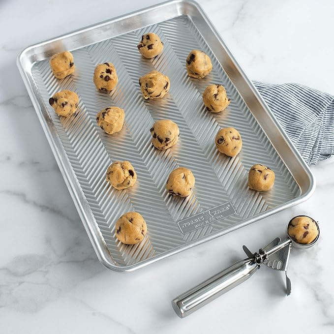 Nordic Ware Small Cookie Dropper, displayed on a baking sheet, ensures uniform 2–3 inch cookies with its ergonomic, 1.5-tablespoon stainless steel scoop for easy baking.