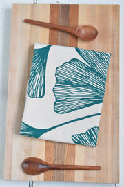 Hearth and Harrow Ginkgo Leaf Tea Towel in Green - Organic Cotton, featuring a hand-printed ginkgo design, lies folded on a wooden surface.