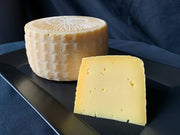 Tulip Tree Creamery - Milkweed: 5 oz. Wedge, a washed rind Alpine-style cheese on a black plate, showcasing a firm yet creamy texture, ideal for melting.