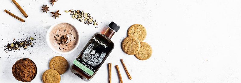 Runamok Peppermint Bark Organic Maple Syrup 250ml surrounded by cinnamon, star anise, chai spices, a spiced beverage, cocoa powder, and ginger cookies, evoking cozy holiday vibes.
