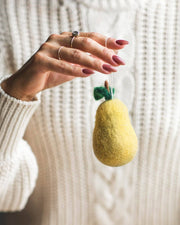Hand holding Farmhouse Pottery - Felted Fruit Ornament: Apple, made from yellow felt, showcasing craftsmanship with delicate rings and knit sweater. Handcrafted in Nepal, Fair Trade Certified.
