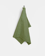 Green linen tea towel hanging on a hook, crafted from high-quality European linen, designed for durability and absorbency in kitchen tasks.