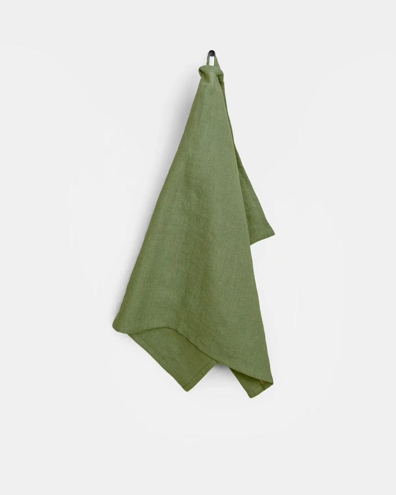 Green linen tea towel hanging on a hook, crafted from high-quality European linen, designed for durability and absorbency in kitchen tasks.