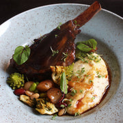 Braised lamb shank with creamy mashed potatoes and vegetables, drizzled with Giusti Quarto Centenario Balsamic Vinegar, highlighted by microgreens garnish.