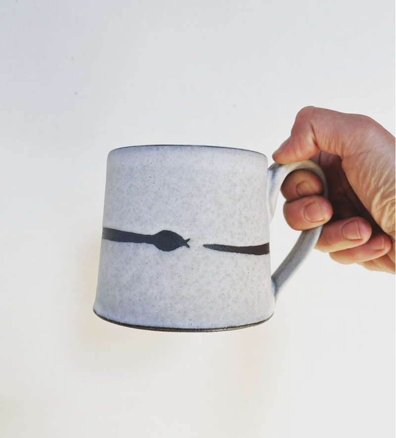 Hand holding Jessica Wertz Ceramics - Ourobouros Snake Mug, featuring a handmade design with irregular black brushstroke on light-gray ceramic, ideal for kitchen enthusiasts.