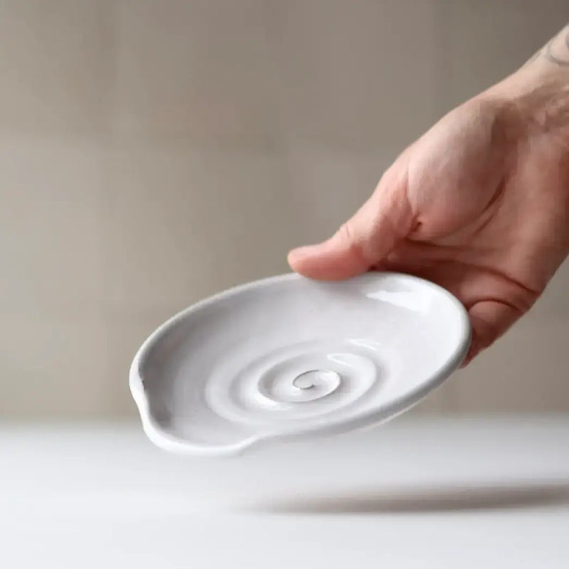 Hand holding a Gravesco Pottery handmade ceramic spoon rest, featuring a spiral pattern and pouring lip, ideal for keeping cooking utensils tidy.