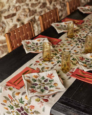Coral & Tusk - Pressed Leaves Dinner Napkin, featuring intricate autumn leaf motifs, elegantly folded atop a pale pink plate in a rustic dining setup.