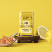 The French Farm - A l'Olivier Lemon From Nice Olive Oil 8.4oz tin with fresh lemons and garnished fish cubes on a wooden board.