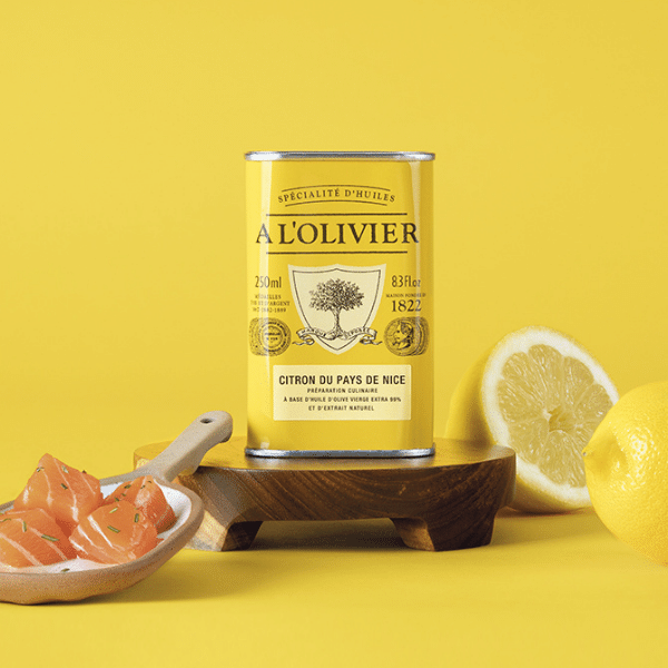 The French Farm - A l'Olivier Lemon From Nice Olive Oil 8.4oz tin with fresh lemons and garnished fish cubes on a wooden board.