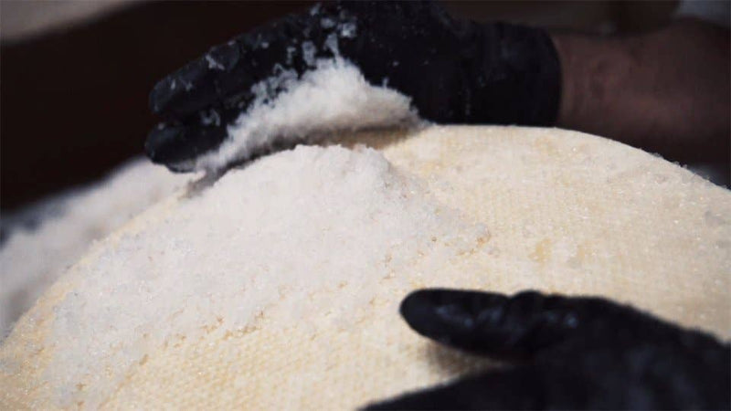 Nicola's Marketplace - Genuine Fulvi® Pecorino Romano DOP: 7 Ounces; black-gloved hands sprinkle salt over a large, round cheese wheel with a dimpled rind.