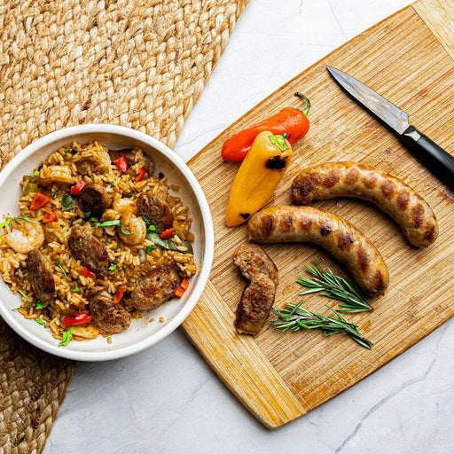 Rock House Creamery | Andouille Sausage - Links displayed beside a knife and a bowl of rice with meat and vegetables, highlighting its gourmet appeal.