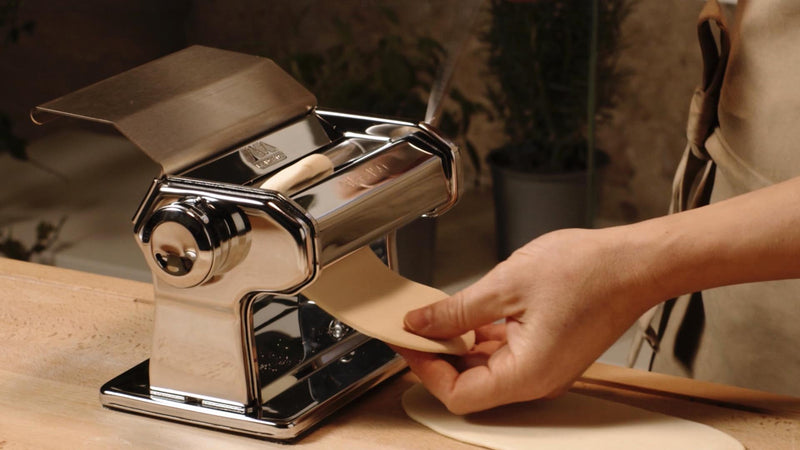 Marcato | Atlas 150 Pasta Maker (Ice) shown for rolling and cutting pasta dough, highlighting its manual operation and adjustable thickness dial for homemade pasta.