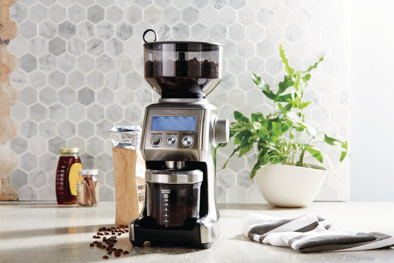 Breville | Smart Grinder Pro on a kitchen counter, surrounded by coffee beans, cinnamon sticks, and a honey jar, highlighting its bean-to-cup grinding capability.