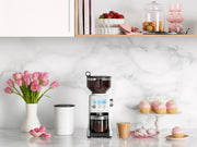 Breville Smart Grinder Pro on a marble kitchen counter, surrounded by coffee beans, pastries, and floral decor, showcasing its versatility and elegance from Athens Cooks.