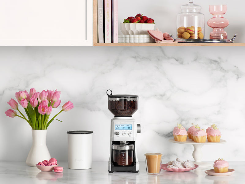 Breville Smart Grinder Pro on a marble kitchen counter, surrounded by coffee beans, pastries, and floral decor, showcasing its versatility and elegance from Athens Cooks.