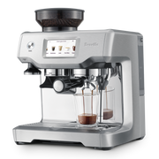 Breville | Barista Touch espresso machine with bean hopper, grinder, and touchscreen showing drink options. Features portafilter, dual-spout for espresso shots, and steam wand for milk frothing.