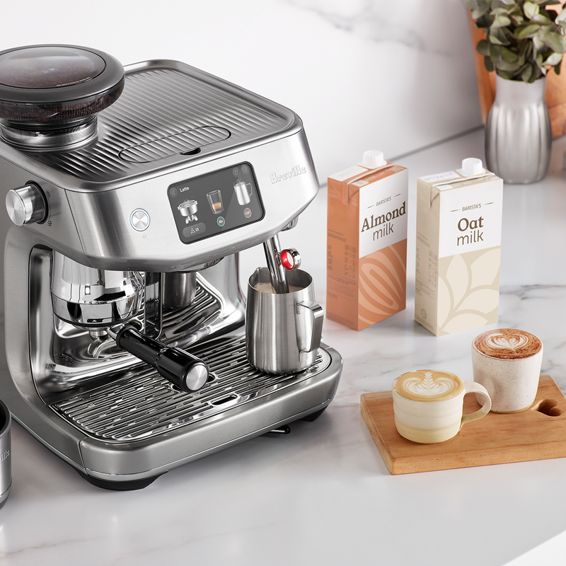 Breville | The Oracle Jet espresso machine with built-in grinder and steaming wand, surrounded by almond and oat milk cartons, two lattes on a tray.