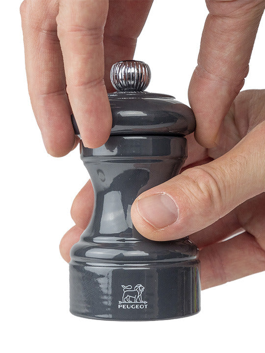Peugeot | Bistro Salt Mill, Slate, in use; a sleek, hand-held grinder with fingers ready to twist, showcasing its timeless design and high-performance mechanism.