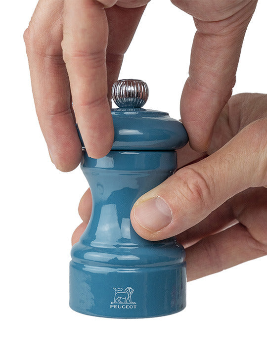 Hands adjust the top of a Peugeot | Bistro Salt Mill, Pacific Blue, showcasing the modern, French-crafted design with a grind level knob for efficient salt milling.