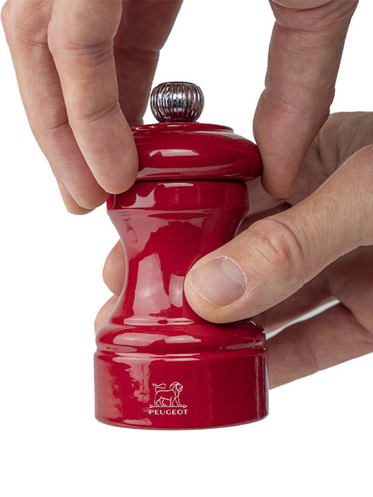 Peugeot | Bistro Salt Mill, Passion Red, being used to grind spices with a twistable top knob for adjustable coarseness, embodying French craftsmanship and elegance.