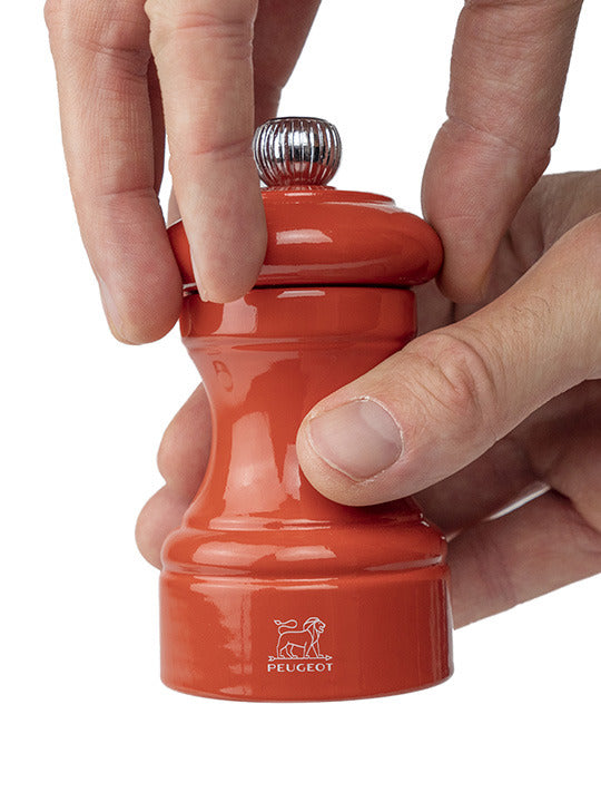 Peugeot | Bistro Salt Mill in terracotta, held in two hands, showcasing its glossy finish and Peugeot lion logo, ideal for grinding salt with precision.