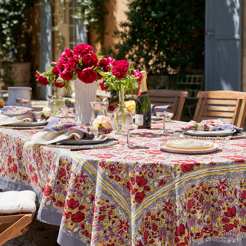 Caravan Home | 71 x 106 Red & Grey Tablecloth displayed on a table, featuring a floral design and surrounded by elegant tableware and a vase of flowers.