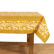 Forest Harvest Grey & Mustard Tablecloth, featuring a hand-printed fruit and foliage design, displayed on a wooden table. Crafted by artisans for Athens Cooks.