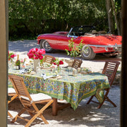 Caravan Home 71 x 71 Jardin Blue & Vert Tablecloth elegantly drapes an outdoor table, adorned with chairs and vibrant pink flowers, embodying luxurious Southern French garden style.