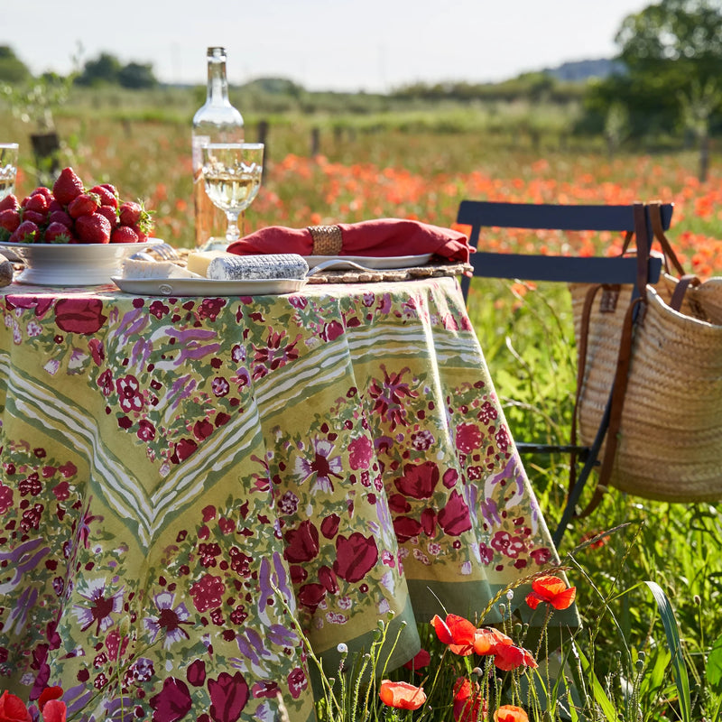 Caravan Home 71 x 71 Red & Green Tablecloth draped on an outdoor table in a field of flowers, part of the Jardin collection.