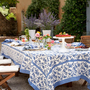Caravan Home | 71 x 106 Granada Cornflower Blue Tablecloth on a party-ready table with floral decor and vibrant tableware.