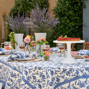 Granada Cornflower Blue Tablecloth elegantly drapes a table set for a party, showcasing intricate floral patterns amidst wine glasses and floral centerpieces.