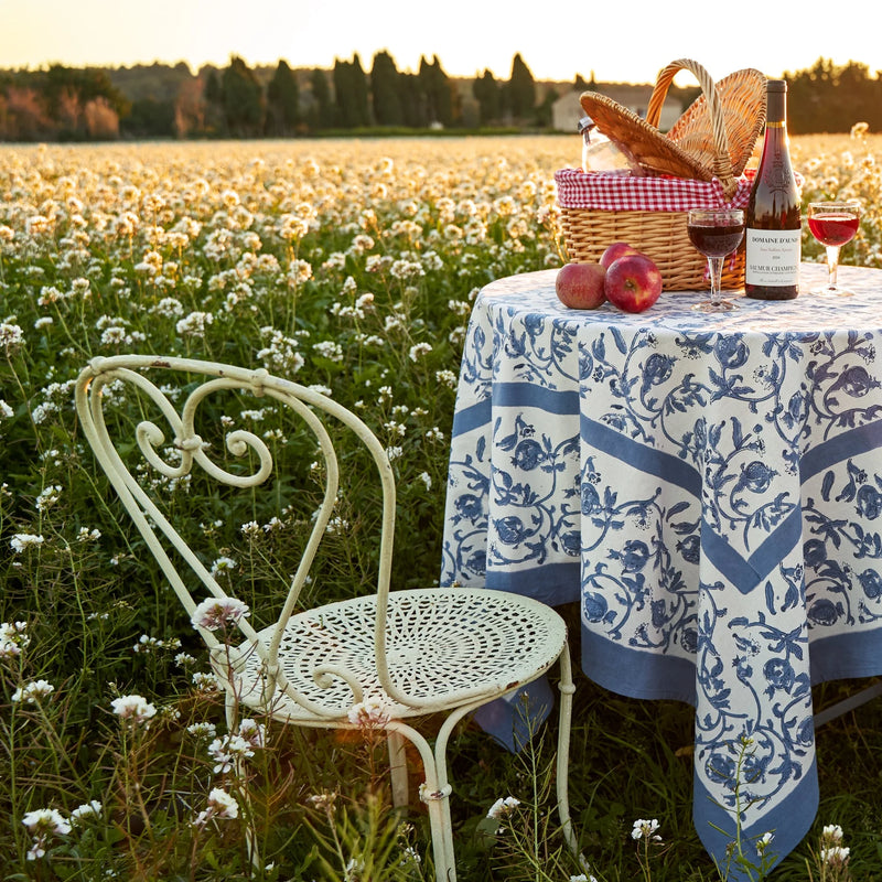 Granada Cornflower Blue Tablecloth on a picnic table in a field of flowers, featuring intricate floral patterns, part of Athens Cooks' curated kitchen collection.