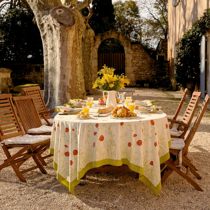 Caravan Home 71 x 106 Springfields Multi French Tablecloth set on an outdoor dining table, accented with a vase of yellow flowers, evoking Provençal charm.