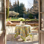 Caravan Home 59 x 86 Jardin Blue & Vert Tablecloth, elegantly draped on an outdoor table with chairs, featuring a floral arrangement in a white pitcher.
