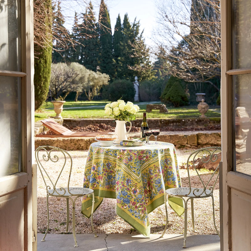Caravan Home 59 x 86 Jardin Blue & Vert Tablecloth, elegantly draped on an outdoor table with chairs, featuring a floral arrangement in a white pitcher.