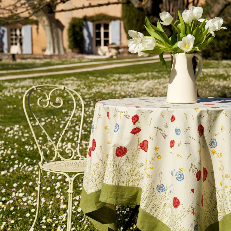 Caravan Home 59 x 86 Springfields Multi French Tablecloth displayed outdoors, adorned with floral designs, complementing a yard setting with a chair and vase.