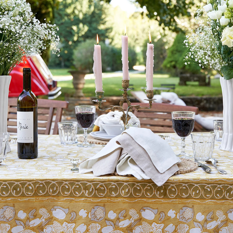 Caravan Home | 71 x 71 Forest Harvest Grey & Mustard Tablecloth, featuring lush fruit and foliage, adorns an elegant table setting with wine and candles.