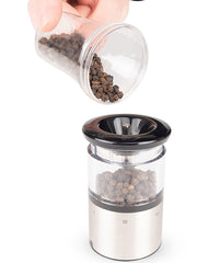 Peugeot Elis Sense Pepper Mill, 8, being filled with black peppercorns, showcasing its sleek stainless steel and acrylic design, ideal for precise, high-tech grinding.