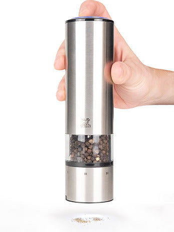 A hand uses the Peugeot | Elis Sense Duo electric spice grinder, releasing freshly ground pepper, highlighting its innovative touch-activation and precision coarseness control.