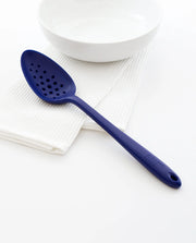 GIR Perforated Spoon on white bowl, showcasing its seamless design and efficient straining holes, perfect for modern kitchen tasks.