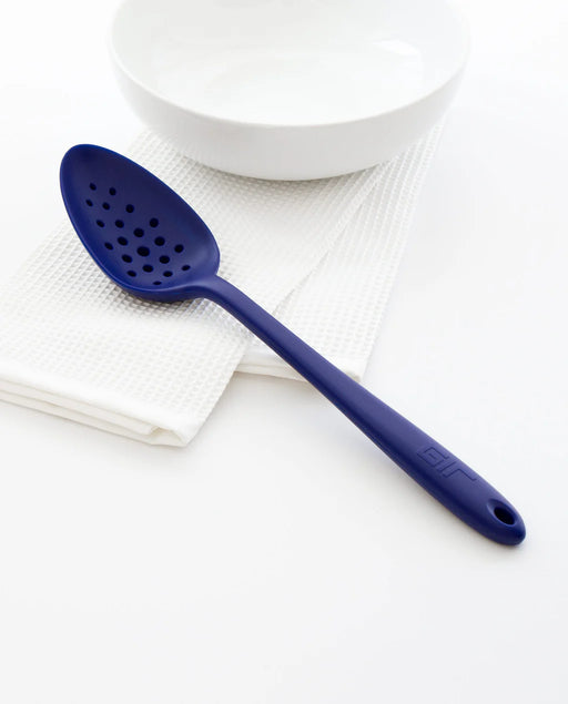 GIR Perforated Spoon on white bowl, showcasing its seamless design and efficient straining holes, perfect for modern kitchen tasks.