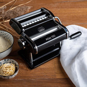 Marcato | Atlas 150 Pasta Maker (Ice) on a wooden surface, accompanied by a bowl of flour, showcasing its manual pasta-making capabilities for homemade Italian pasta.
