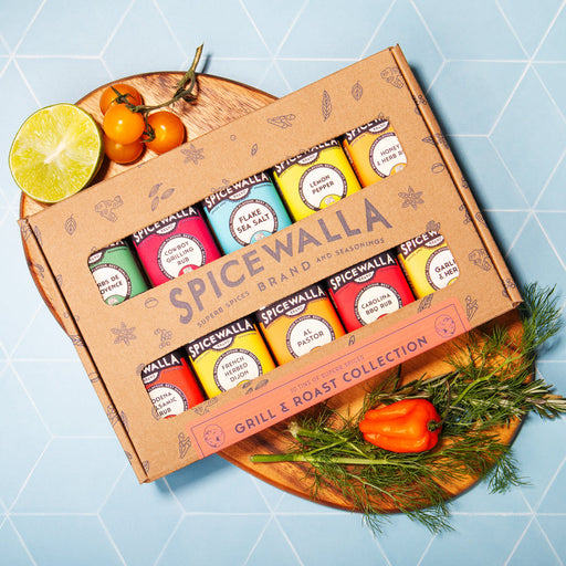 Spicewalla | Grill & Roast Gift Collection: Ten-pack of seasonings including Cowboy Grilling Rub and Herbs de Provence, arranged with garnishes on a wooden board.