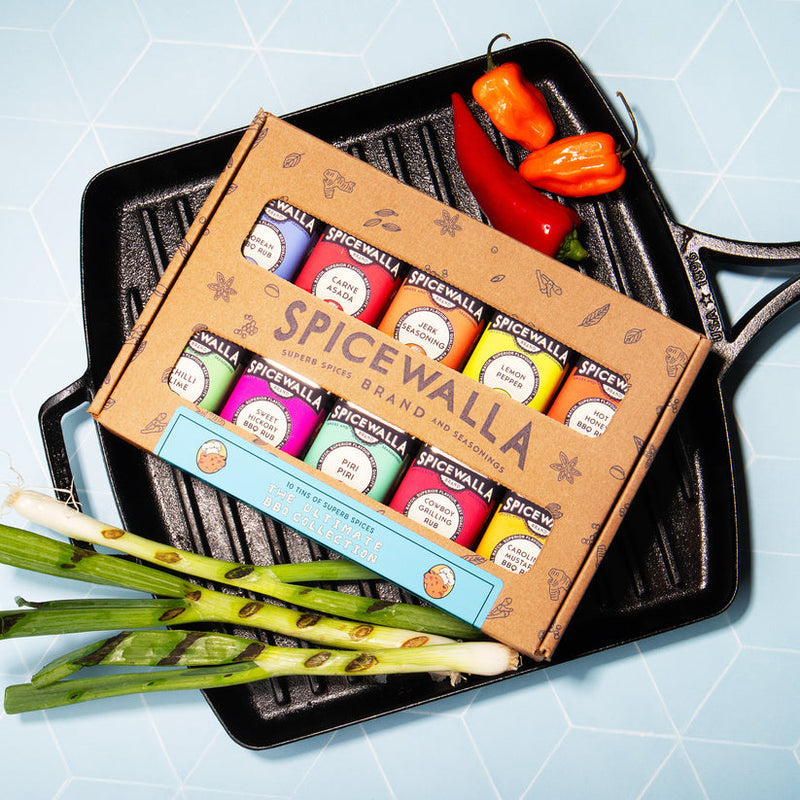 Spicewalla | Ultimate Backyard BBQ Collection, 10 Pack, in a grill pan with mini spice tins labeled for various BBQ blends, surrounded by chile peppers and scallions.