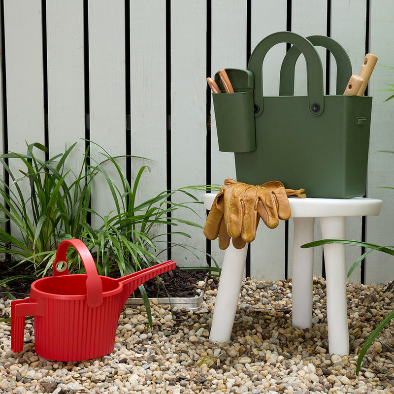 Hachiman | Garden Tool Bag Garden Green on a white stool, holding gardening tools, beside a red scooping container on gravel, ideal for organized garden work.