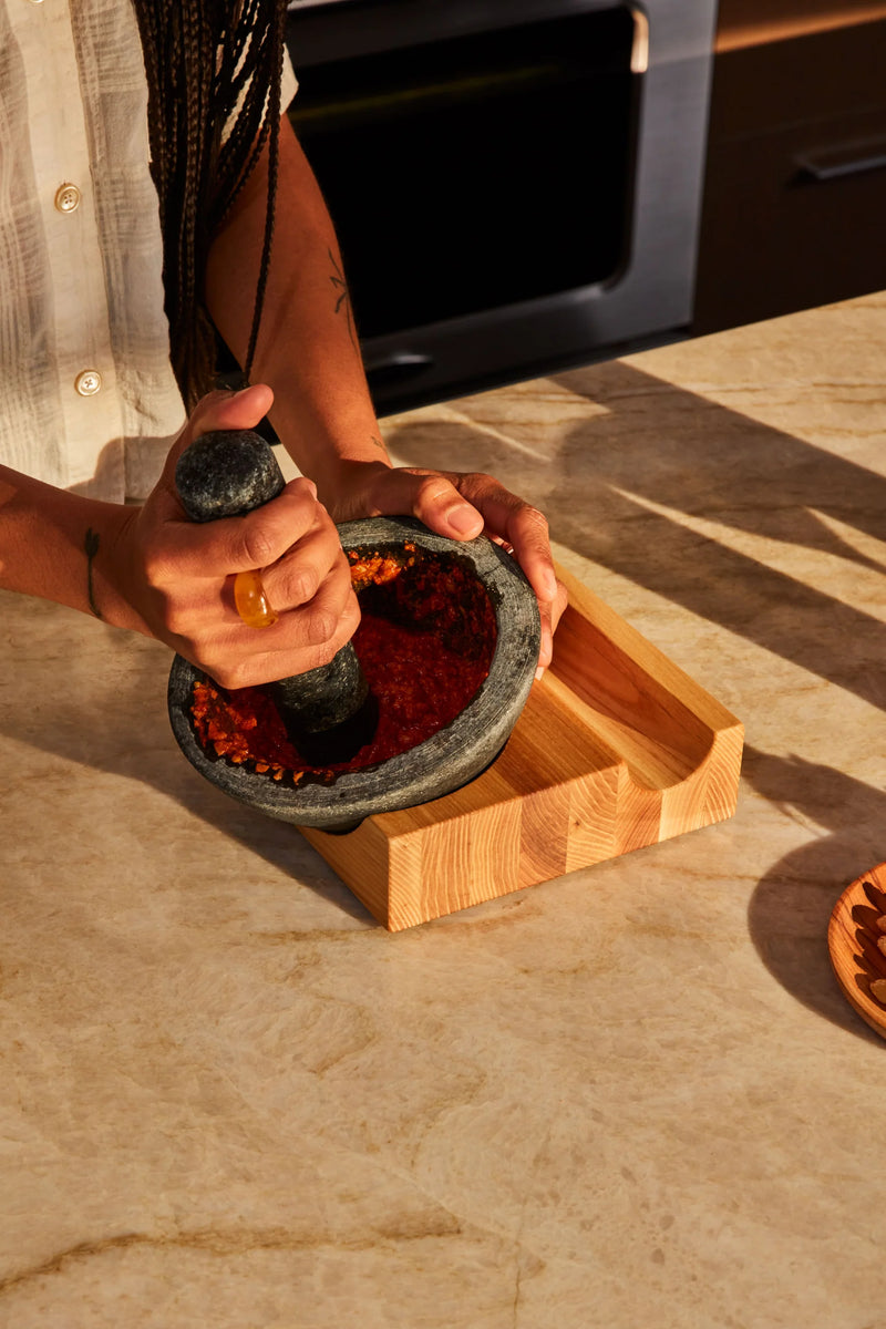 Holcomb Studio | Perch Mortar & Pestle in use, showcasing its granite texture and ash wood base, ideal for grinding spices and enhancing kitchen craftsmanship.