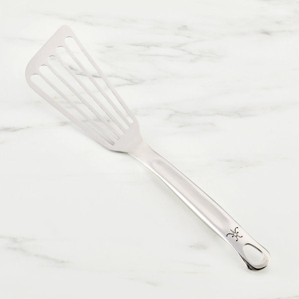 Hestan | Stainless Steel Flexible Fish Spatula, 13 lying on a marble surface, showcasing its sleek design and versatility for precise cooking tasks.