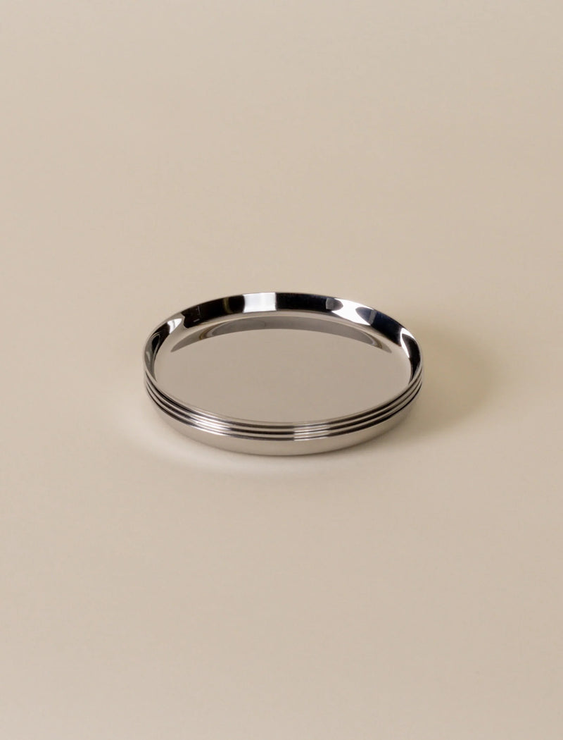 Holcomb Studio Puddle Coasters, Set of Four: Polished stainless steel coasters with anti-slip pads, designed to protect surfaces from condensation and spills, stackable for easy storage.