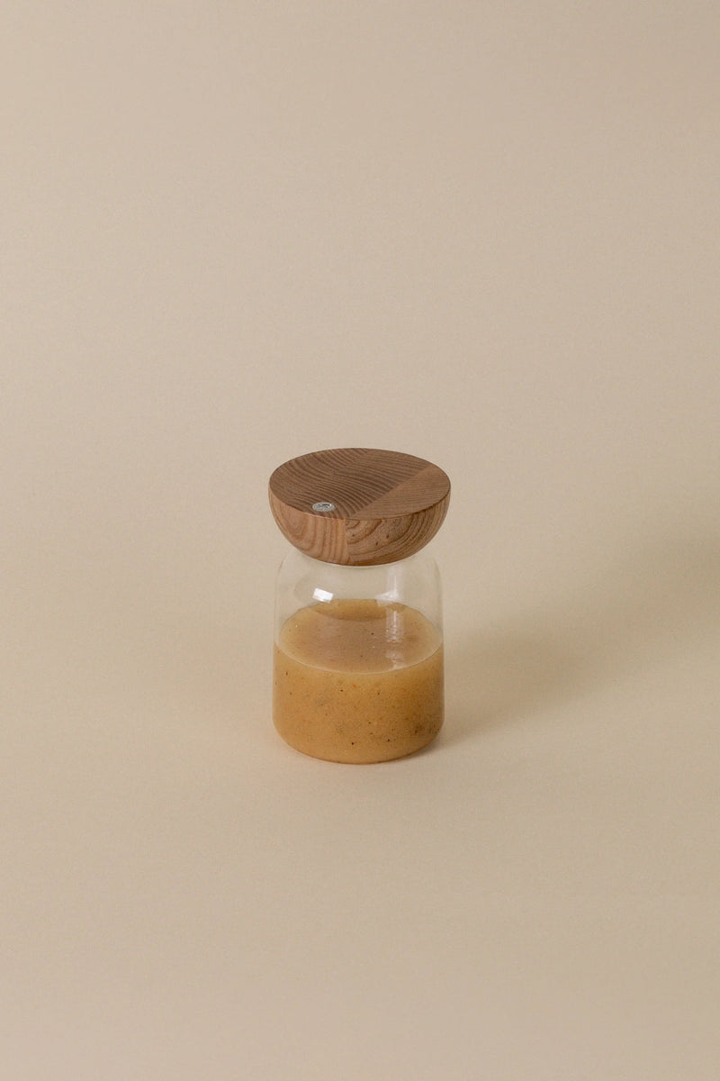 Holcomb Studio | Totter Salad Dressing Shaker: A glass jar with brown liquid and a wooden lid, ideal for mixing and serving dressings.