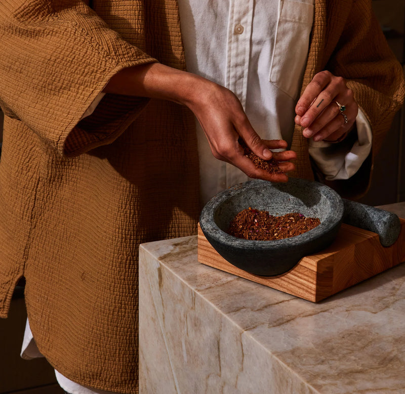 Holcomb Studio | Perch Mortar & Pestle in use, showcasing its granite stone and ash wood base design for grinding spices, reflecting Athens Cooks' curated kitchen essentials.